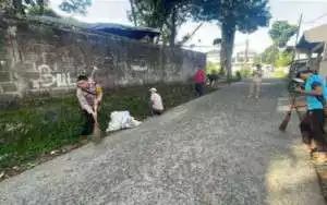 Bhabinkamtibmas Polsek Ciawi gotong royong bersama warga Desa Banjarwangi membersihkan jalan lingkungan.